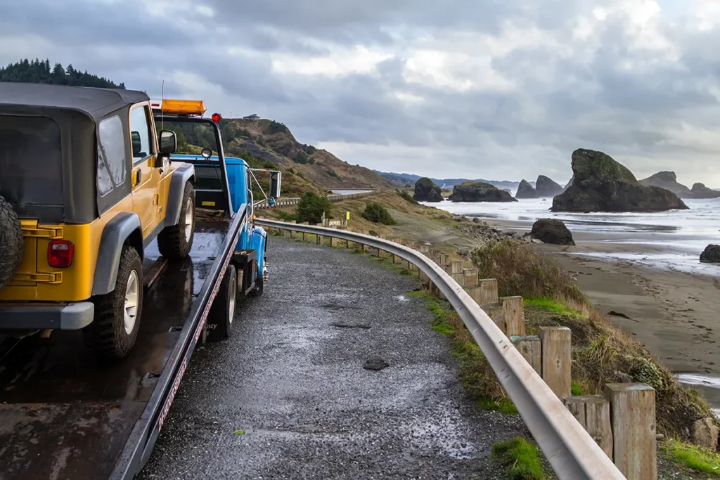 Jeep on the back of a tow truck at a beach